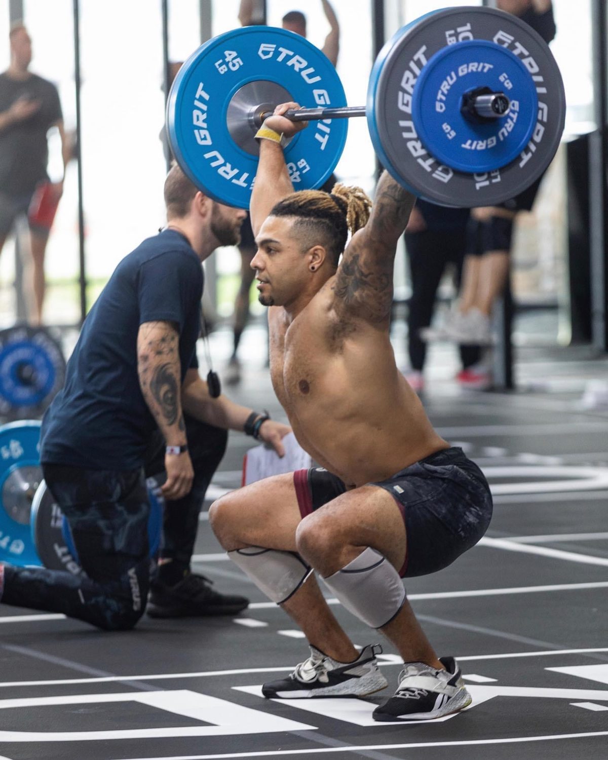 Coach Daimino Stewart holding a barbell overhead in a squat